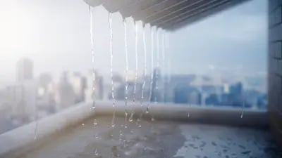 Water droplets cascading from a rooftop onto a rain-soaked surface with a city skyline in the background. 