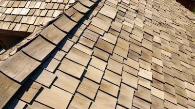 A close-up view of a wooden shingle roof with a weathered, natural finish under sunlight. 