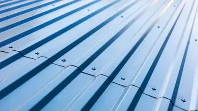 Close-up of blue metal roofing panels, showcasing ridges and screws, ideal for construction and renovation projects. 