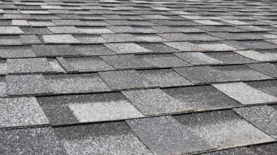 Close-up of a textured asphalt shingle roof with gray tones and overlapping patterns. 