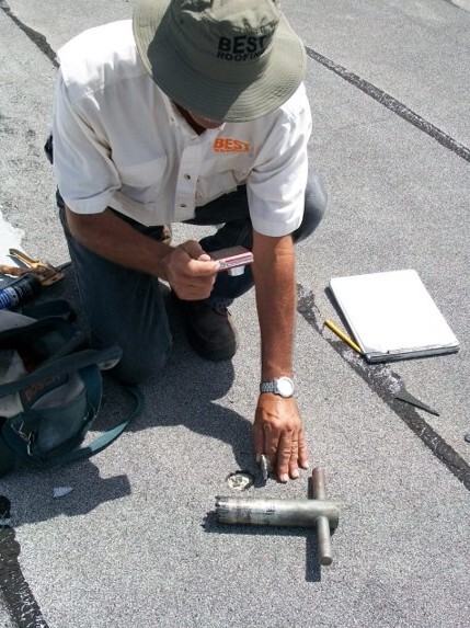 A technician inspecting roofing materials and using a smartphone on a rooftop. 