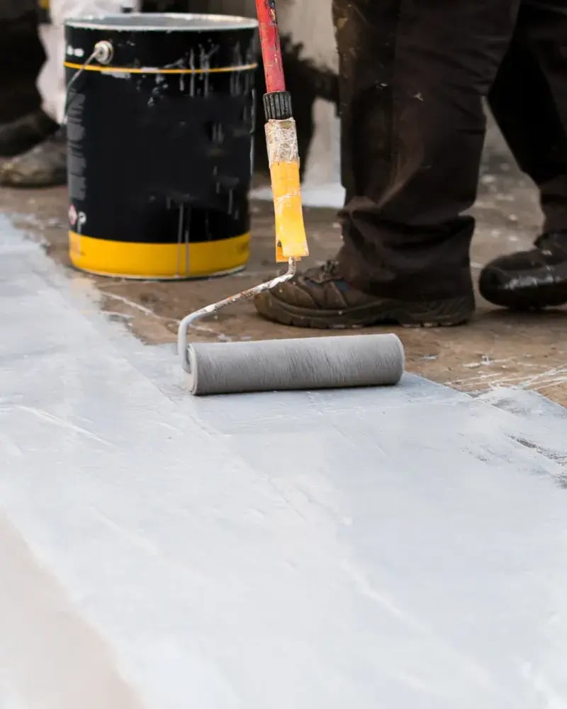 A roofing contractor applying product with a rolling brush to a concrete roof.