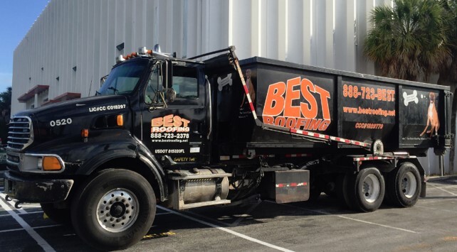 Black dump truck with advertising for Best Roofing parked outside a building.